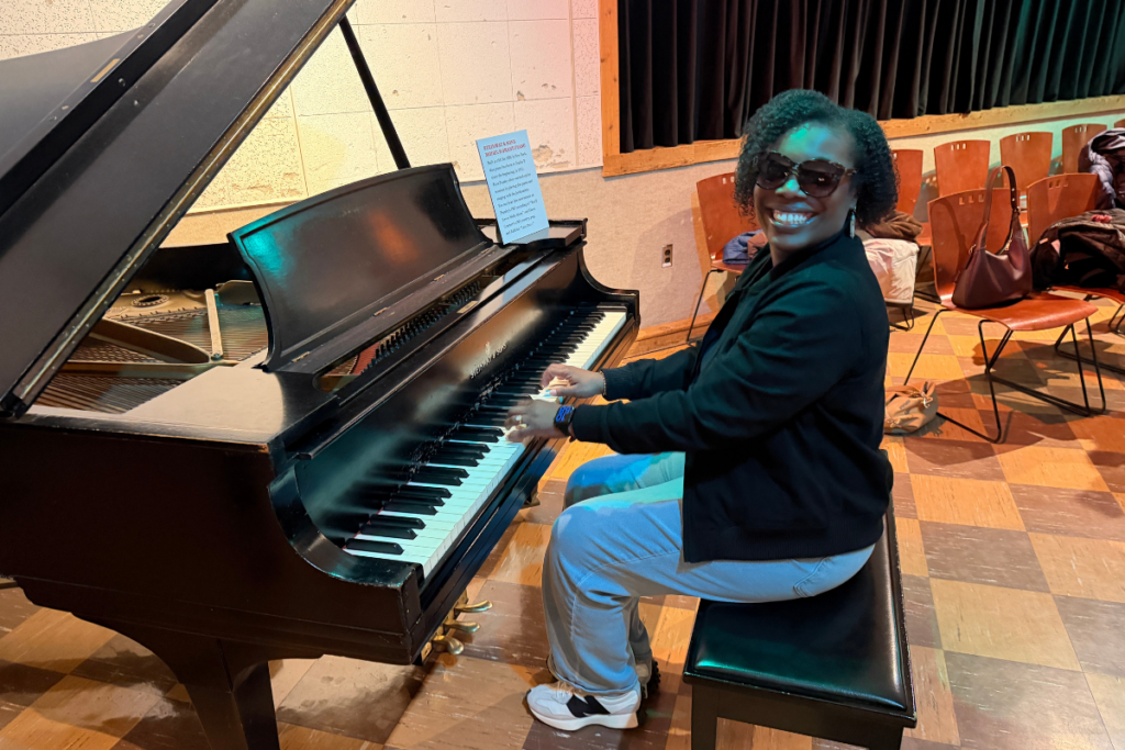 Woman sitting at piano wearing sunglasses and smiling.
