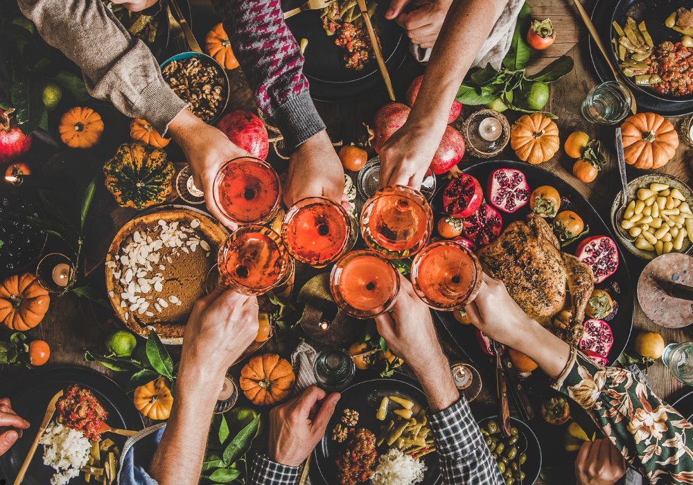 Overhead view of friends toasting a drink over thanksgiving foods. 
