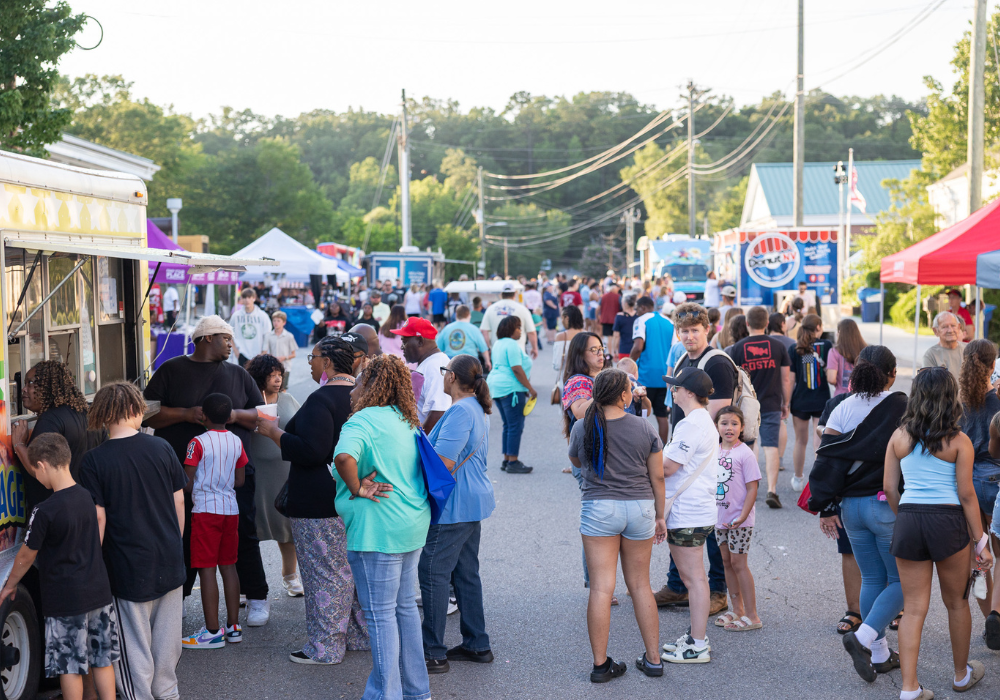 A large crowd of families and attendees lines up at food trucks and vendor booths along a downtown Pell City street during the annual Pell City Block Party.