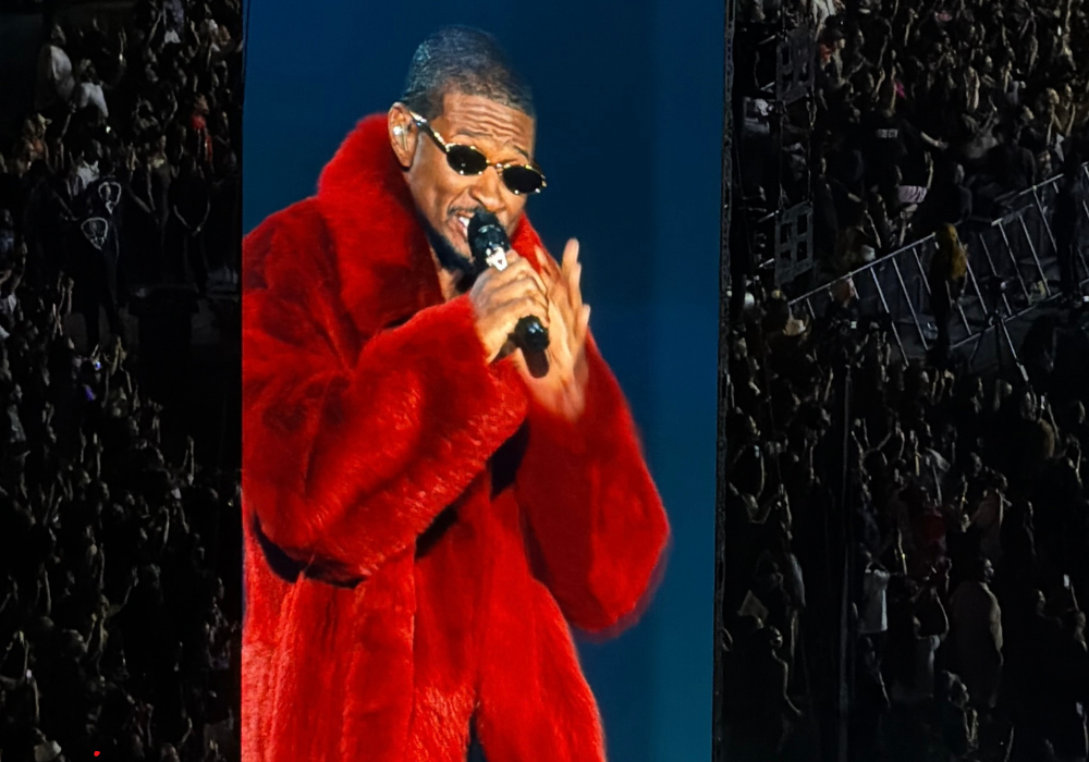 Usher performing in a red fur coat on the jumbotron screen at Protective Stadium during the R&B Tour.